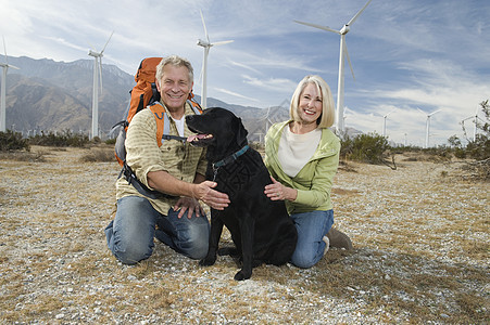 在风力农场附近带狗的老年夫妇能源远足衬衫环境问题环保享受服装涡轮机宠物退休图片
