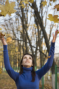 公园中落树叶下的妇女乐趣树木中年服装休闲享受微笑黑发衣物女性图片