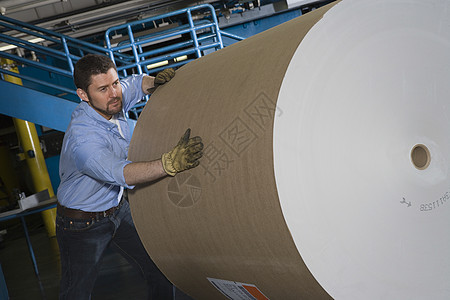 男人在报纸工厂里 推着一卷巨大的纸图片