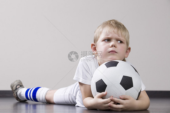 男孩躺在地板上 拿着足球球肖像头发沉思爱好服装影棚童年青春期运动表情倾斜图片