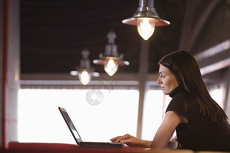 在咖啡馆使用膝上型电脑的年轻妇女活动棕色人士咖啡店商务轮用技术女性前景桌子图片