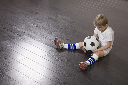 坐在地板上拿着足球球的男孩图片