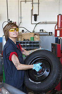 一名自信的年轻女机械工在汽车修理车间内搬运轮胎的肖像图片