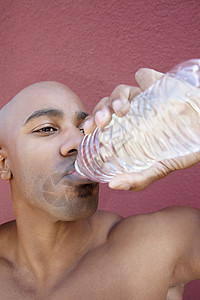 非裔美国青年男子饮用瓶装加彩色本底的饮用水图片