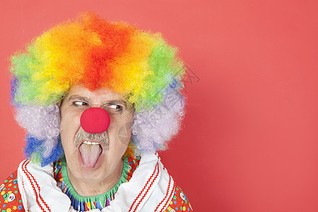 高年的男小丑伸出舌头 一边看红背景 一边仰视着红色背景图片