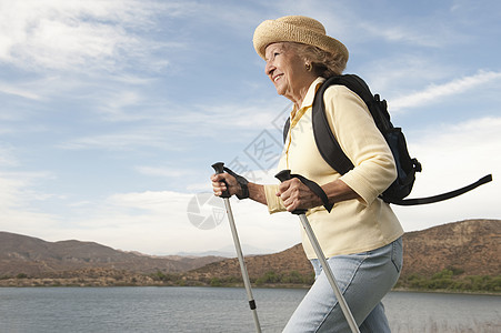 高级女性与行走杆一起学习天空太阳帽休闲牛仔裤背包多云精力草帽手杖服装图片