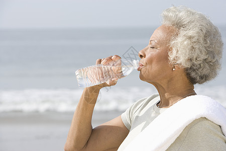 在沙滩上看到高龄妇女用毛巾套在肩上的饮用水的侧边景象图片