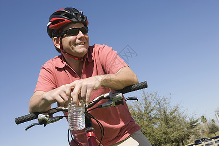 骑自行车头盔的成年男子靠着自行车把手栏图片