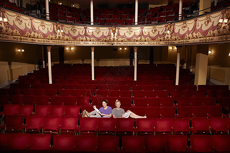 两名年轻女青年坐在戏剧摊位的全长肖像 手持剧本图片