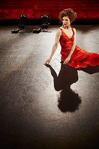 穿着红袍的年轻美女坐在舞台地板上图片