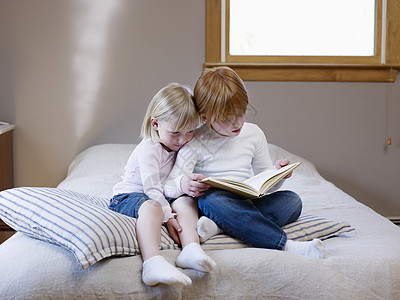 两姐妹坐在单张床上看书牛仔裤卧室服装时间家庭头发窗框闲暇孩子们软垫图片