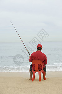 坐在红塑料椅上 在海滩钓鱼的红色T恤男子的近视图片