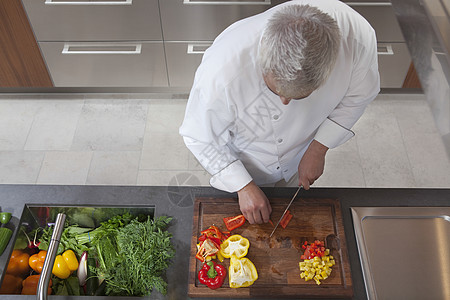雄厨师在商业性厨房中切红和黄胡椒的高角角视角图片