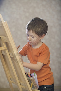 一个小男孩站在画布的边缘 用一罐彩色铅笔在画布上作画绘画孩子孩子们神童画架童年塑料男孩们艺术家创造力图片
