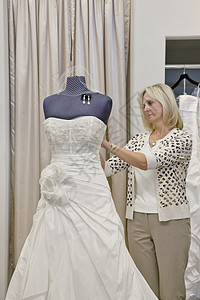 高级女业主调整婚纱在新娘店的模特儿上的婚纱图片