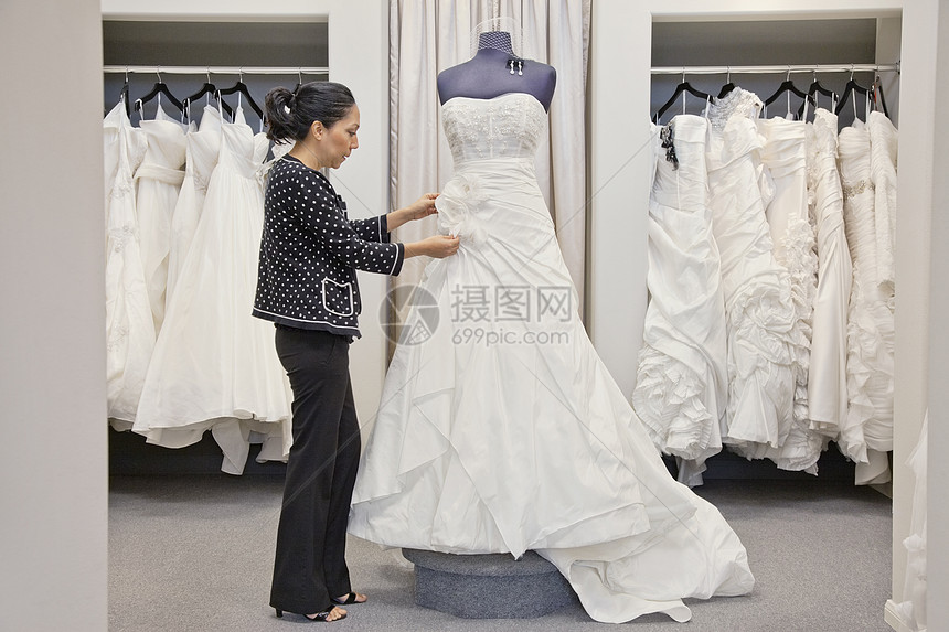 一家成熟雇员在新娘商店调整优雅婚纱的侧面视图图片