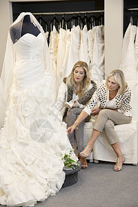 美丽的年轻女士和母亲坐在一起 看着新娘店的结婚礼服;以及图片