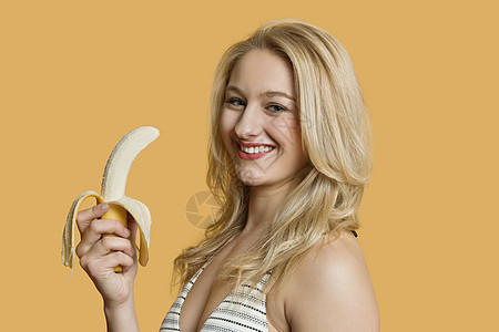 一位年轻女子在彩色背景上吃香蕉的肖像图片