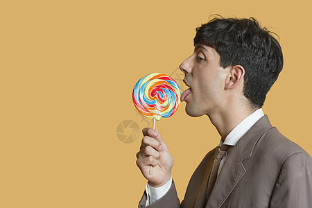 在彩色背景上舔棒棒棒糖的年轻商务人士的侧面视图图片