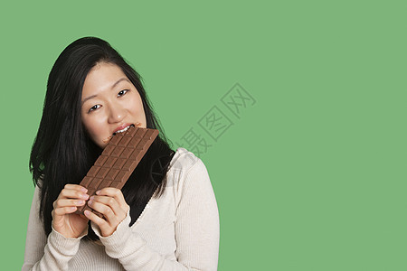 一位年轻女子在绿色背景下吃大巧克力条的肖像图片