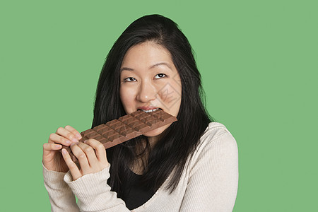 在绿色背景上吃一大块巧克力条的 可爱的年轻女人图片