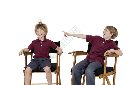 白色背景下坐在导演椅上的青春期前男孩指着朋友的头发背景图片