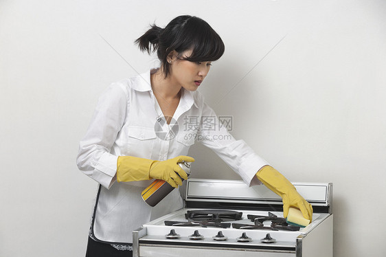 灰色背景的年轻女佣清洁炉灶图片