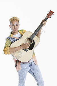在灰色背景下弹吉他的一个少年男孩的肖像图片