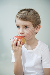 年轻男孩在灰色背景上吃苹果的肖像图片