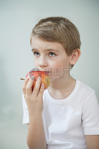 年轻男孩在灰色背景上吃苹果的肖像图片