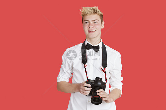 红背景上带有数码相机的英俊年轻男子图片