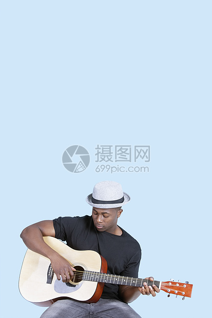 非洲裔美国青年男子在浅蓝背景下弹吉他游戏长度衣服男性音乐乐器成年成人影棚服装彩色图片