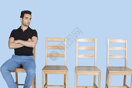 蓝背景坐在空木椅旁的年轻男子的肖像 在蓝色背景之下图片