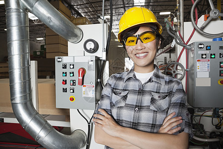 女性工业工人站在有背景机器的工厂里时微笑着笑容的肖像 其背景是图片