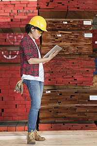 一名亚洲女工业女工使用平板电脑 背着堆叠木木板的侧面视图图片