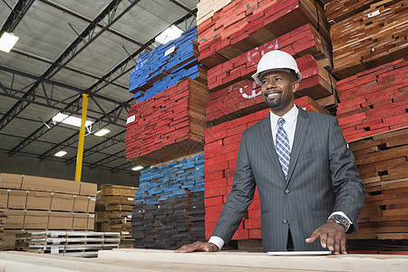 一名非洲裔美国男性承包商站在堆叠木板前的一块木板前面图片