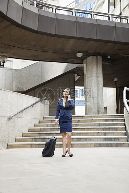 年轻印度女商务人士使用手机和户外行李行李的手提电话图片