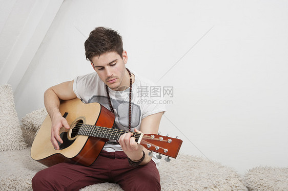年轻的高加索男子坐在草沙发上弹吉他图片