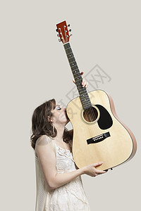 年轻女子在灰色背景下亲吻吉他图片