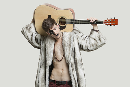 穿着毛皮大衣的年轻男吉他手肖像 在灰色背景下肩扛着吉他图片