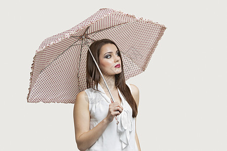 年轻女人拿着伞 却不看灰色背景的眼神图片