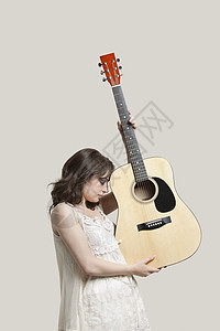 在灰色背景下携带吉他的年轻女子图片