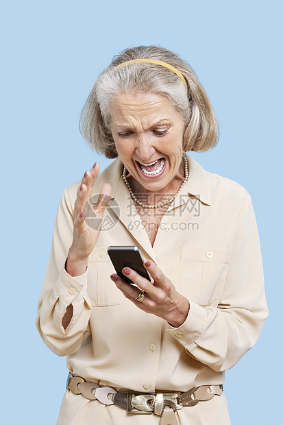 在蓝色背景下在手机上阅读短信的高级女性被激愤起来图片