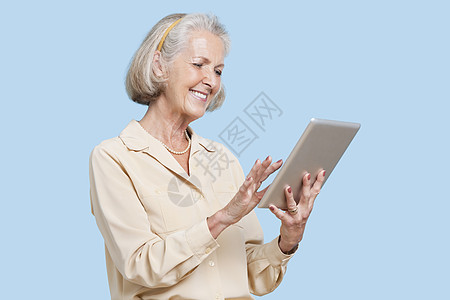 在蓝色背景下使用平板电脑的快乐高级妇女图片