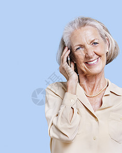 在蓝背景下使用手机微笑的年长妇女 ;图片