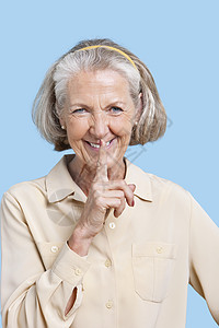 在蓝色背景下 用手指在嘴唇上乱指的散间中微笑着微笑的年长妇女的肖像图片