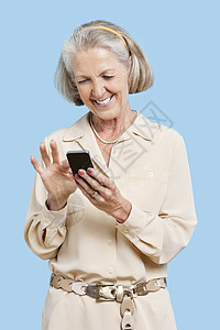 在蓝背景下在手机上读短信的微笑高龄妇女; 以蓝色背景阅读图片