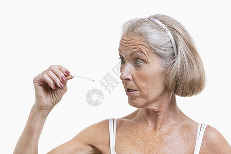 高级妇女对照白色背景检查温度计;高龄妇女图片