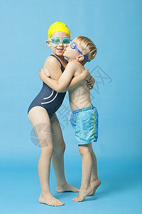 穿着游泳服的年青兄弟姐妹拥抱和接吻蓝底影棚幸福泳帽童年泳镜姐姐闲暇男生蓝色感情图片