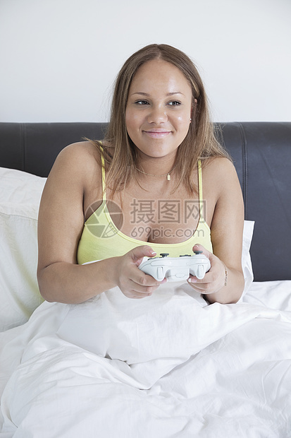年轻怀孕婴儿在床上玩遥控遥控电玩游戏女性成人享受电子游戏毯子家庭娱乐孕产闲暇怀孕图片